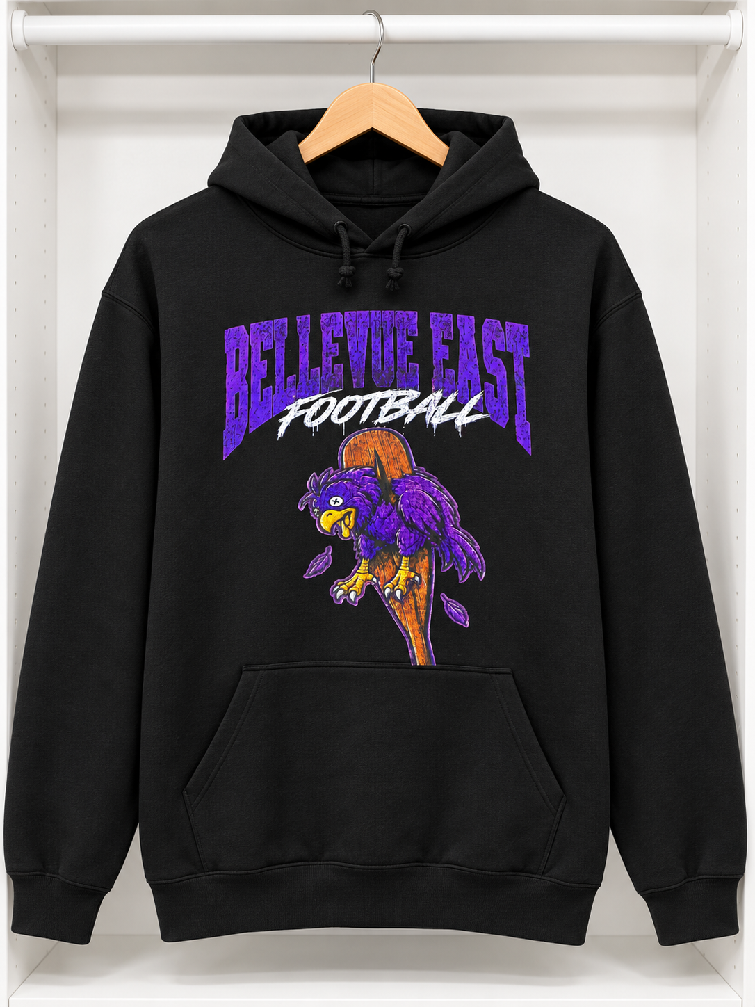 A black pullover hoodie hanging on a wooden hanger against a white wall. The hoodie features a large graphic on the chest with the words 'BELLEVUE EAST FOOTBALL' in purple and white, above a purple and orange football mascot illustration.