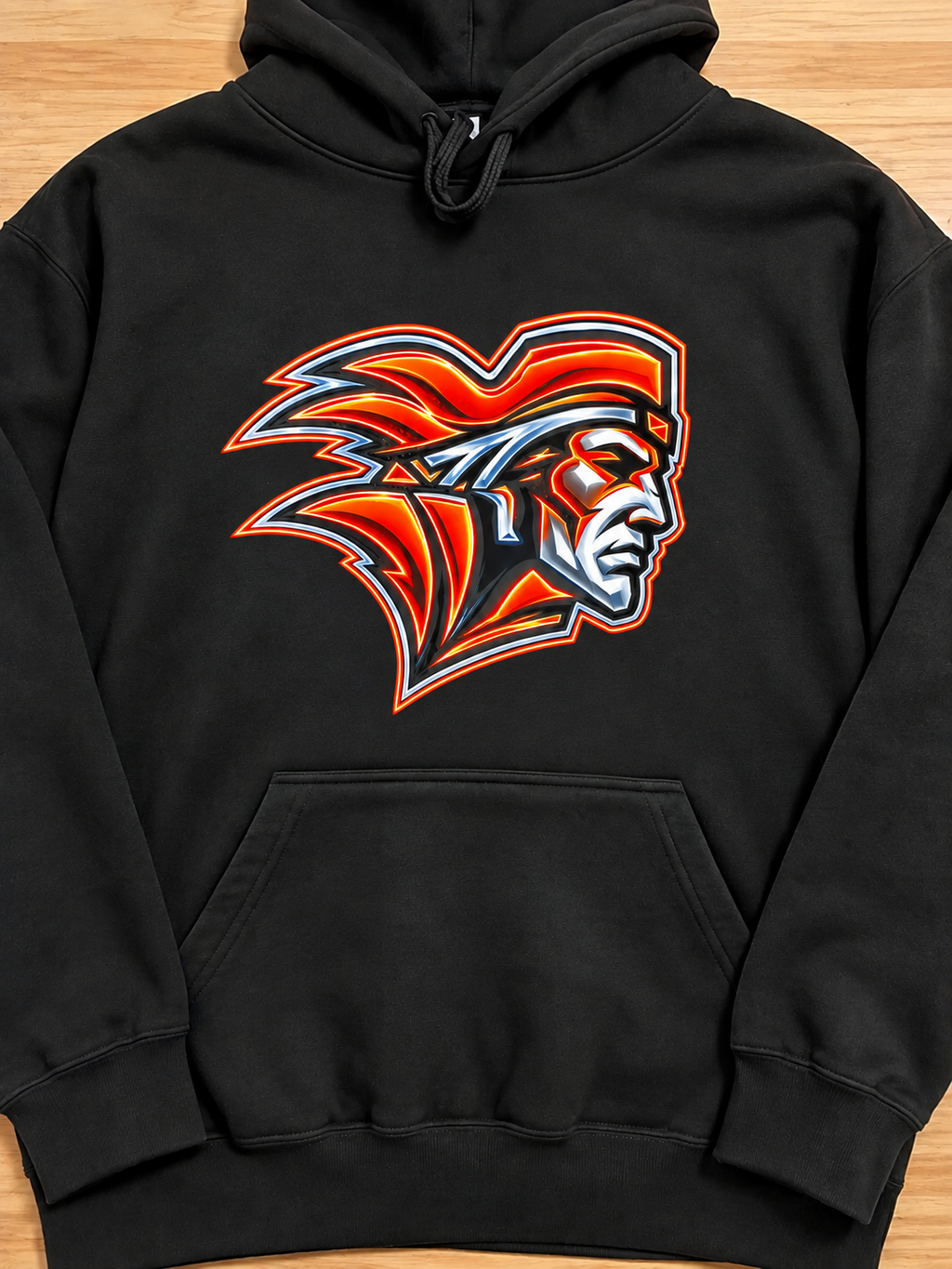A black pullover hoodie laid flat on a light wood surface, featuring a large graphic of a Native American profile in red, orange, white, and black on the chest.